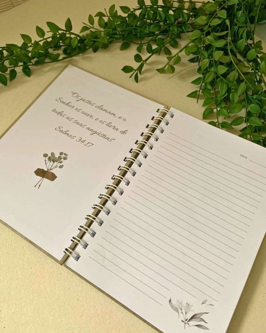 Caderno aberto mostrando o miolo pautado, com o versículo do Salmo 34:17 impresso e ilustração botânica.