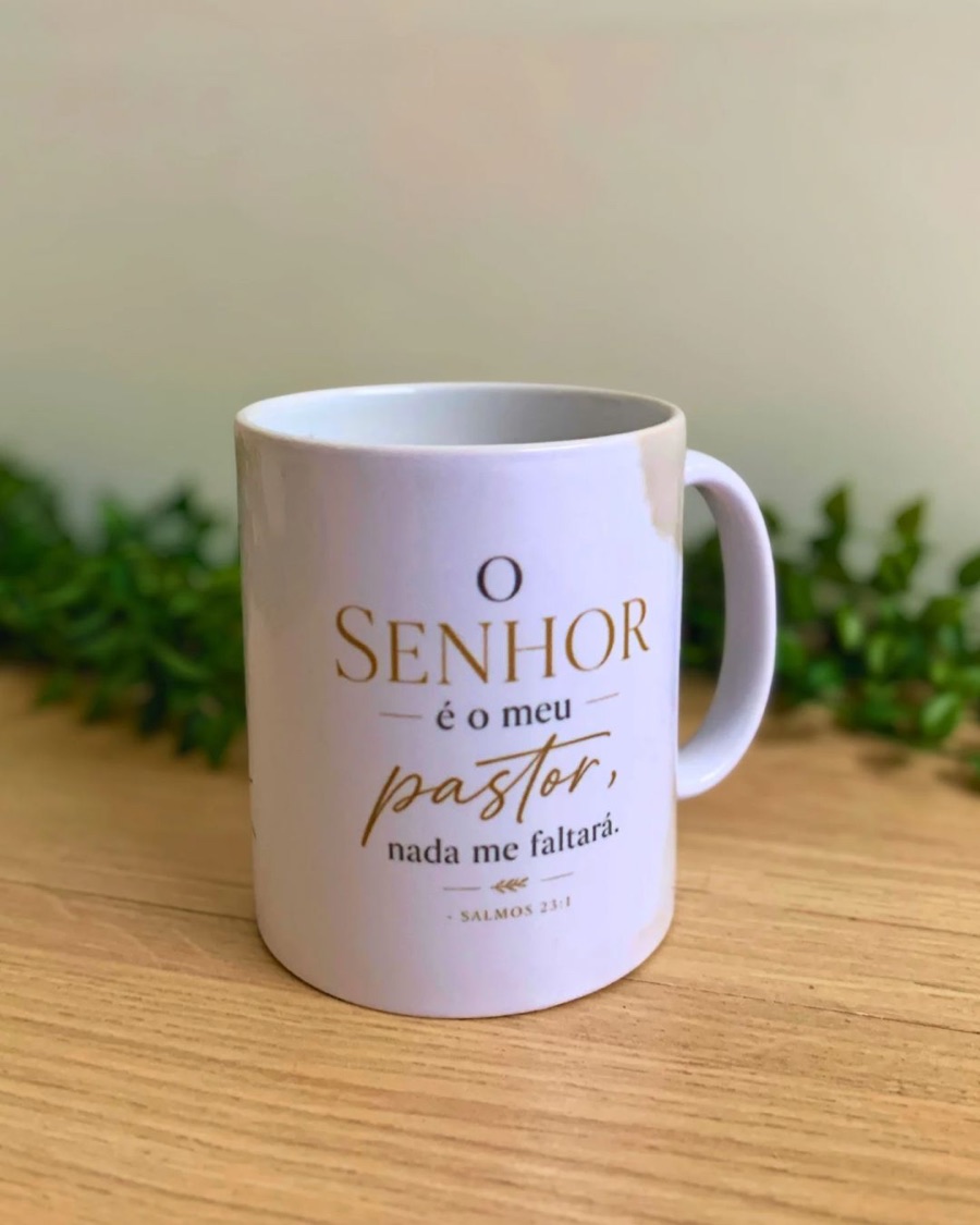 Caneca branca personalizada com o versículo “O Senhor é o meu pastor, nada me faltará”, em letras douradas, sobre mesa de madeira.